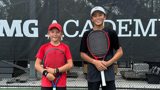 Two young boys pose on court with their tennis racquets