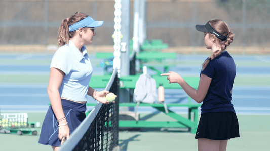Two young girls meet at the net on a tennis court.